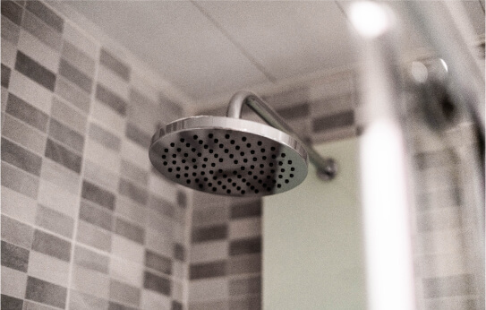 Close up of a shower head in a gray tiled bathroom.