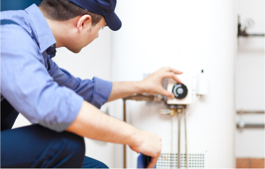 A plumbing technician wearing a blue shirt adjusts a meter by hand.