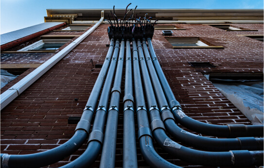 Several pipes running up the side of a brick building.