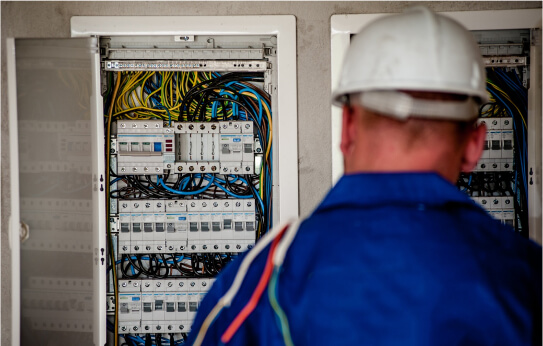 View of an electrician from the back, with an electrical panel in front of them.