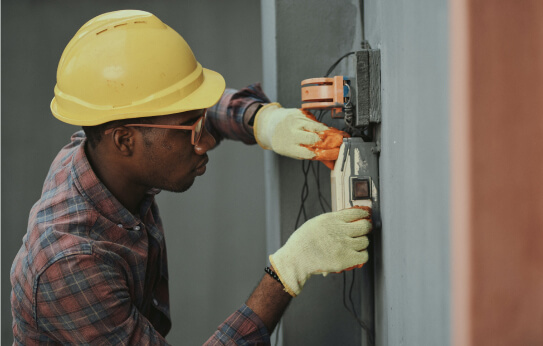 An electrician wearing a hard hat working on an electrical panel.